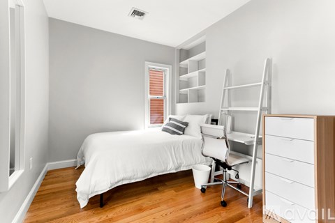 A white bedroom with a bed, chair, and storage unit.
