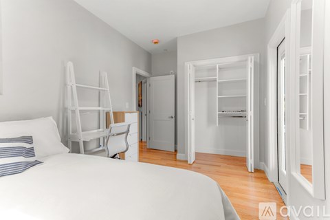 A white bedroom with a bed, chair, and wardrobe.
