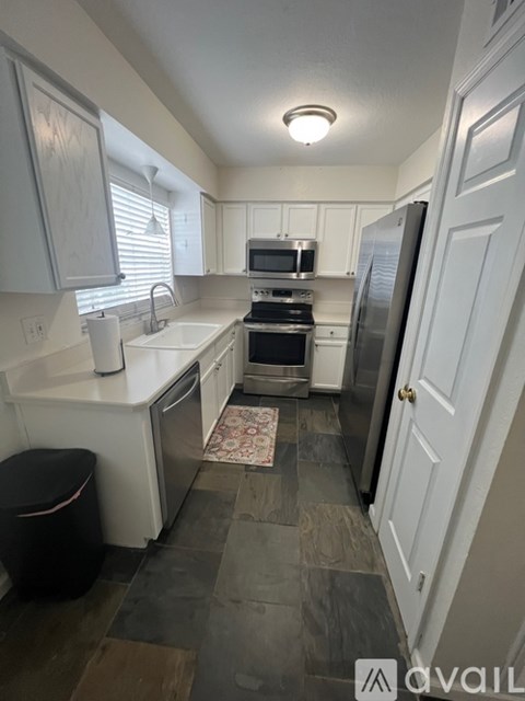 A kitchen with white cabinets and a black trash can.