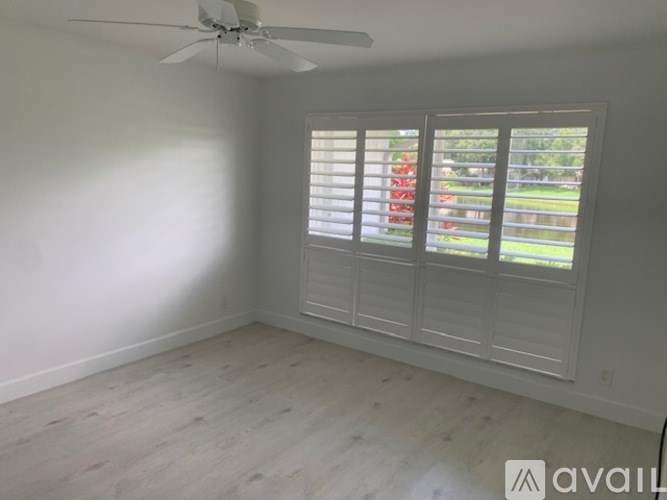 A room with a ceiling fan and a window with white blinds.