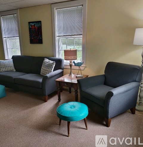 A living room with a grey couch, a grey armchair, a small table with a lamp and a painting on the wall.