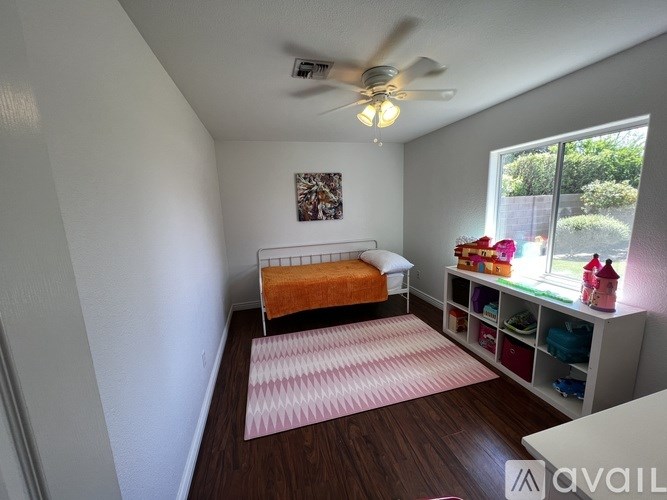 A bedroom with a bed, a fan, and a window with a view of the outside.