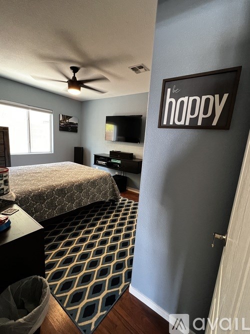A bedroom with a bed, a ceiling fan, and a wall hanging that says "be happy".