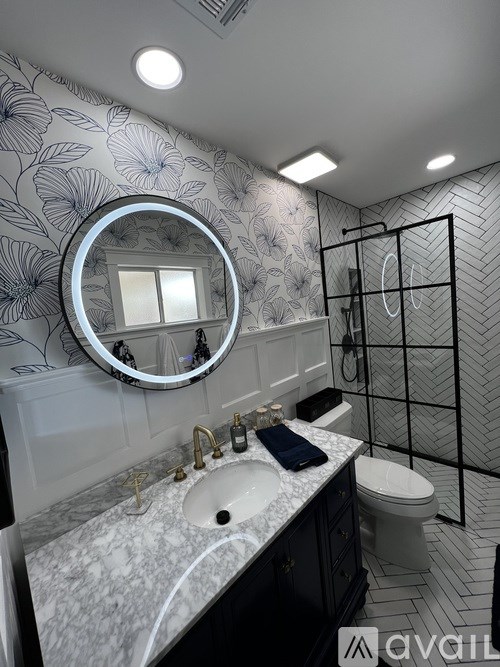 A bathroom with a round mirror, sink, toilet, and a shower with a glass door.