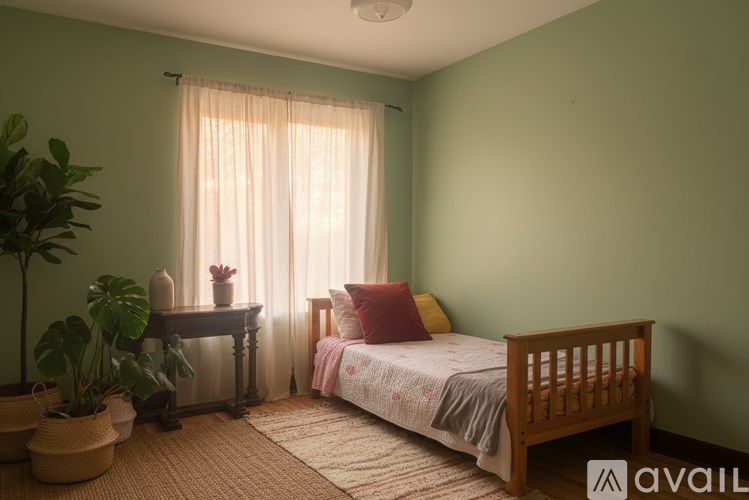 A bedroom with a bed, a table, a window with curtains, and a potted plant.