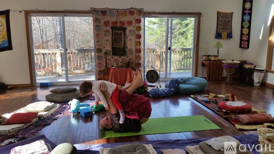 A woman is doing yoga with a child on her lap in a room with a large window.