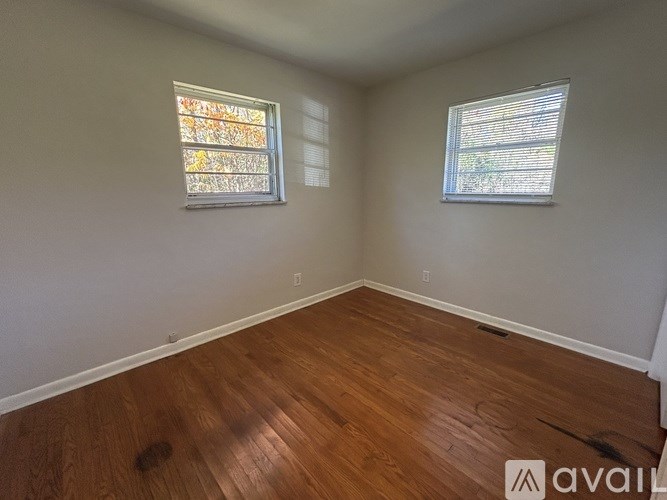 A room with wooden flooring and two windows.