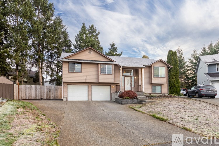 A house with a brown roof and a grey garage door is surrounded by a fence and trees.