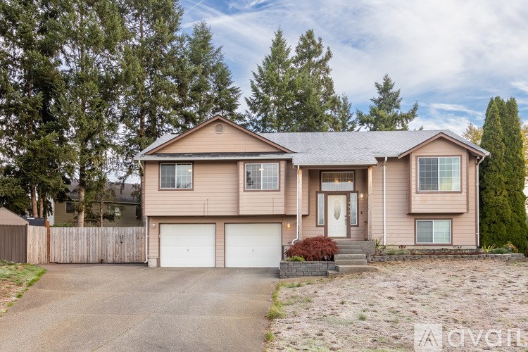 A two-story house with a garage is surrounded by trees and has a driveway in front.