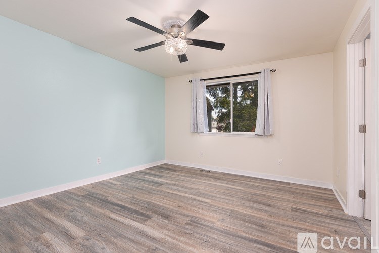 A room with a ceiling fan and a window with curtains.