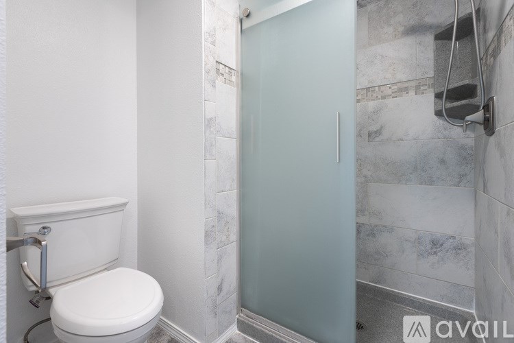 A white toilet with a silver flush handle in a bathroom with a glass shower door.
