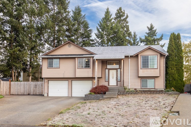 A house with a brown roof and white garage doors is surrounded by trees.