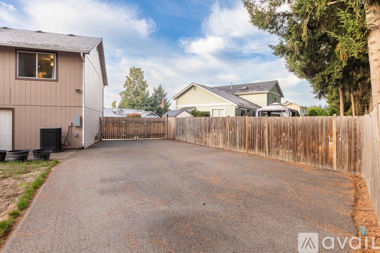A backyard with a driveway, a fence, and a house in the background.
