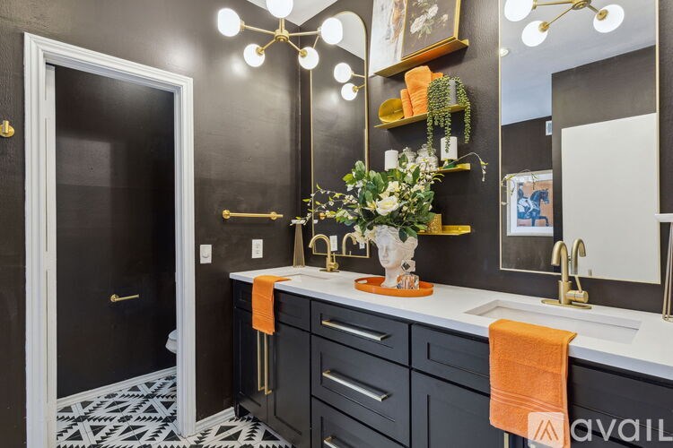 A bathroom with a black and white tiled floor, a sink with a gold faucet, and a mirror above it.