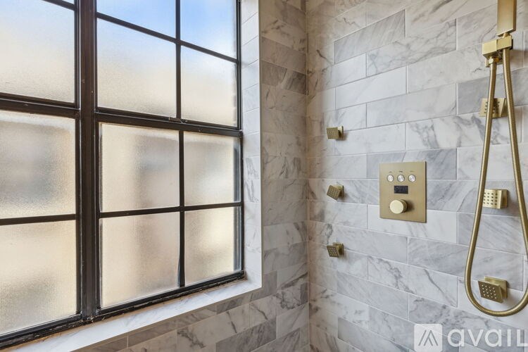 A bathroom with a marble wall and a shower with a gold shower head.