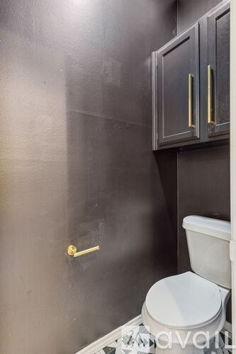 A toilet in a bathroom with a black wall and a gold towel bar.