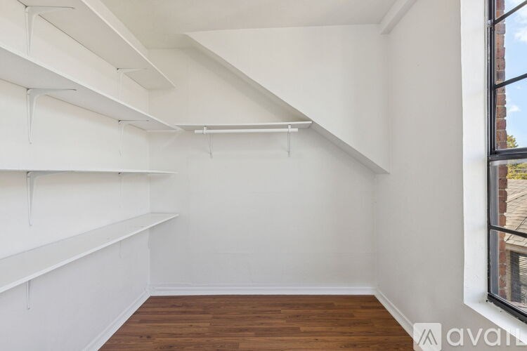 A room with white walls and wooden floors has a large window on the right side.