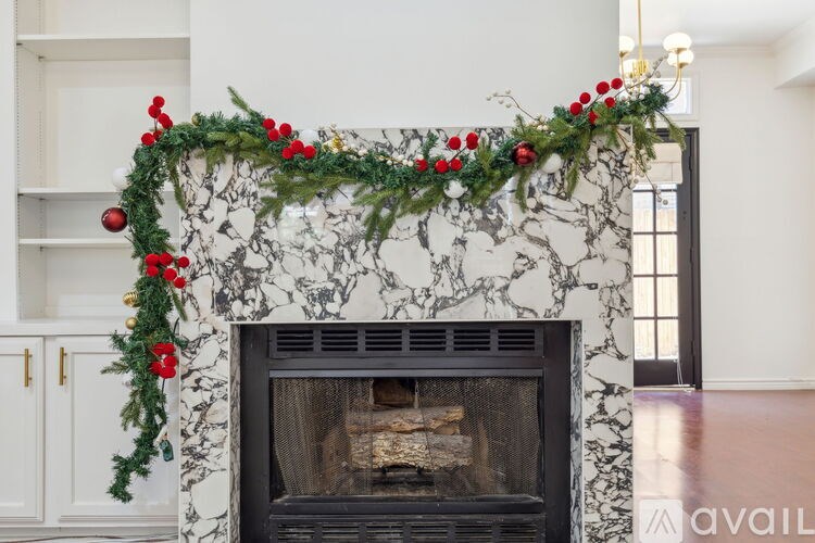 A fireplace with a garland of red berries and green leaves on top of a marble mantle.