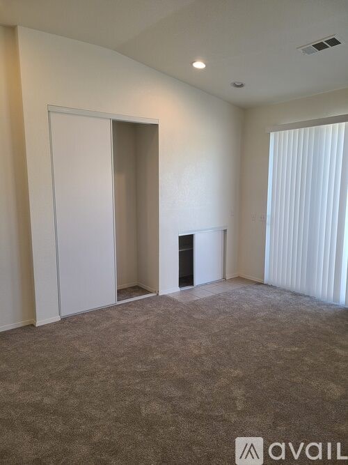 A carpeted room with a door and a window with blinds.