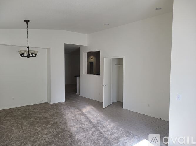 A large, empty room with a chandelier and a carpeted floor.