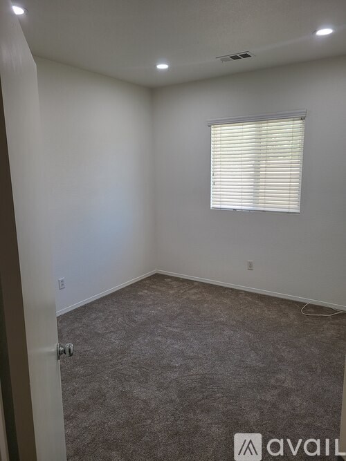 A room with a carpeted floor and a window with blinds.