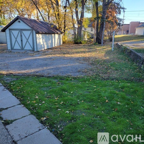 A small white shed with a brown roof is situated in a grassy area with a sidewalk leading up to it.