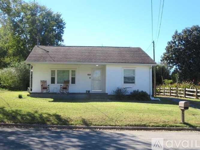 A small white house with a brown roof and a fence in front.