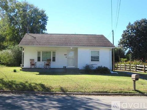 A small white house with a brown roof and a fence in front.