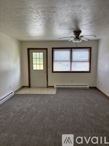 A room with a carpeted floor, a ceiling fan, and a door leading to a balcony.
