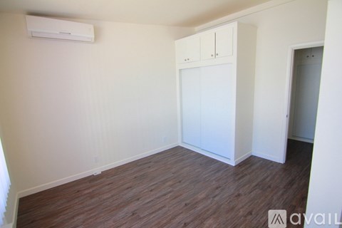 A room with a wooden floor and a white wall with a cabinet and a door.