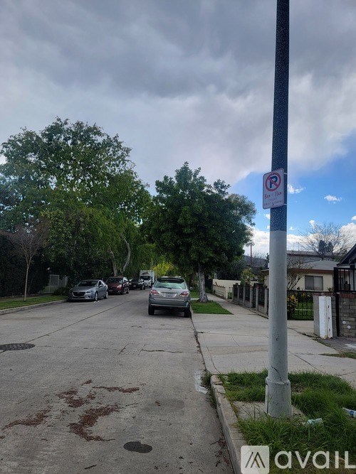 A street with cars parked on the side and a no parking sign on a pole.
