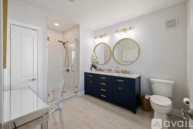 A bathroom with a white toilet, a sink with a mirror and lights above it, and a blue cabinet.