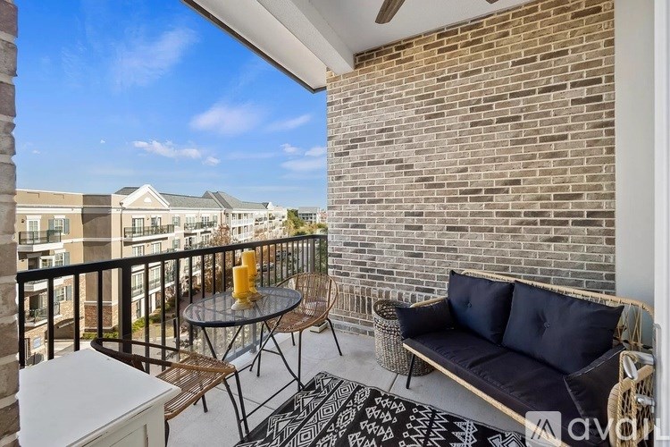 A balcony with a black couch, glass table and chairs, and a brick wall.