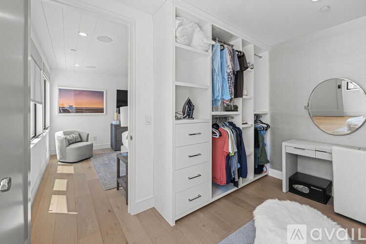 A spacious walk-in closet with white shelves and drawers, a round mirror, and a desk with a chair.