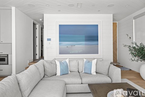 A living room with a grey couch and a large picture of a beach on the wall.