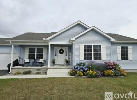 A blue house with a white door and windows, a wreath on the door, and a flower bed in front.