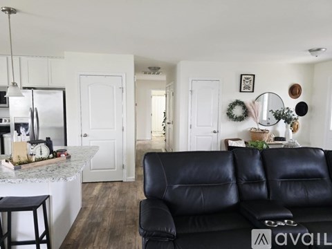 A black leather couch sits in a kitchen with a white counter and a fridge.