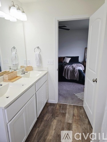 A bathroom with a white sink and mirror, and a bedroom with a bed and ceiling fan in the background.