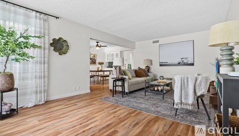 A living room with a couch, a chair, a table, a potted plant, and a painting on the wall.