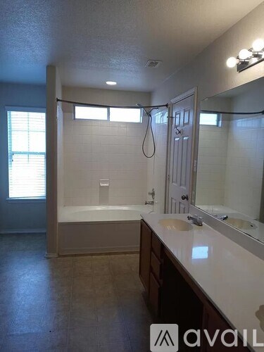 A bathroom with a tub, sink, mirror, and a window.