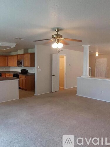 A living room with a ceiling fan and a kitchen area with cabinets and a microwave.