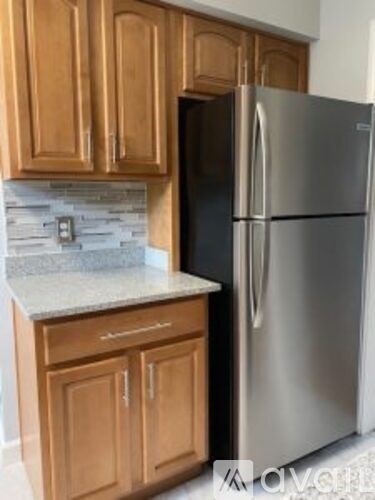 A stainless steel refrigerator stands in a kitchen with wooden cabinets.