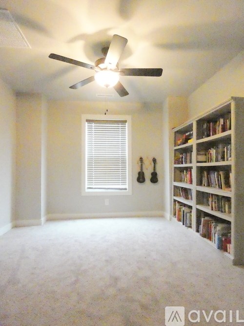 A room with a ceiling fan, bookshelf, and window with blinds.