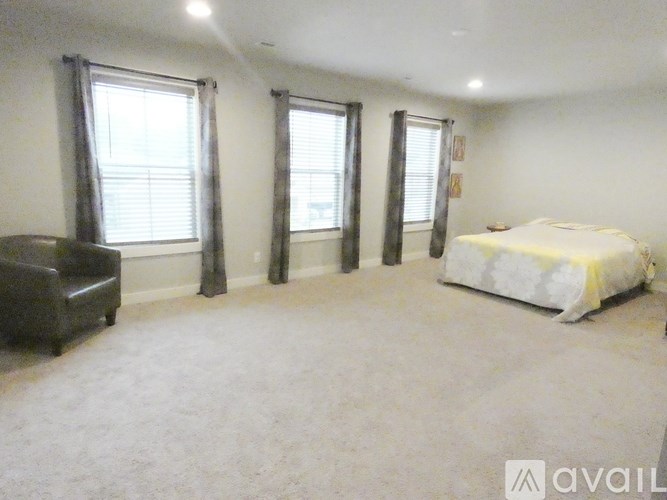 A bedroom with a bed, couch, and two windows.