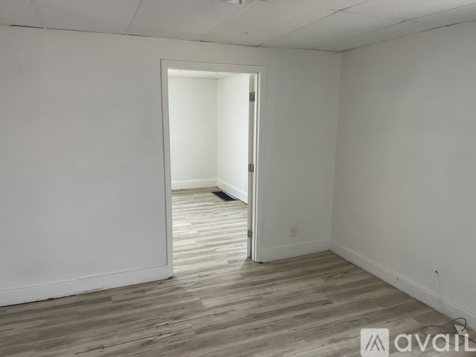 A room with a wooden floor and white walls, with an open door leading to another room.