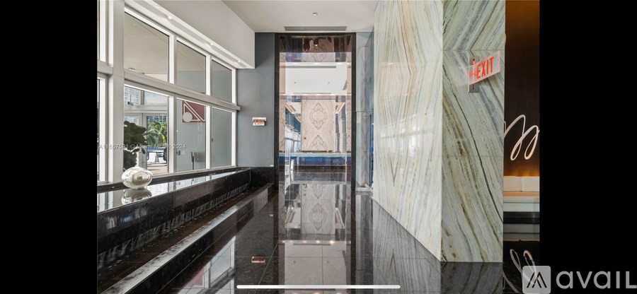 A hallway with a black marble floor and a red exit sign on the wall.