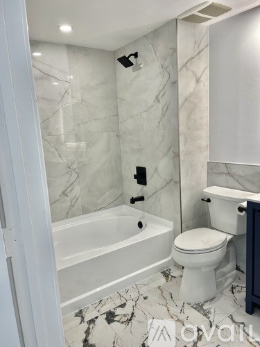 A white toilet sits next to a bathtub in a marble bathroom.