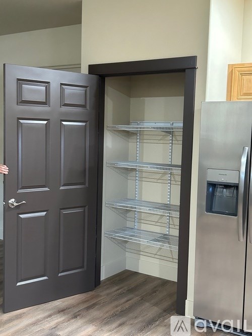 A person is opening a black door to reveal a stainless steel refrigerator.