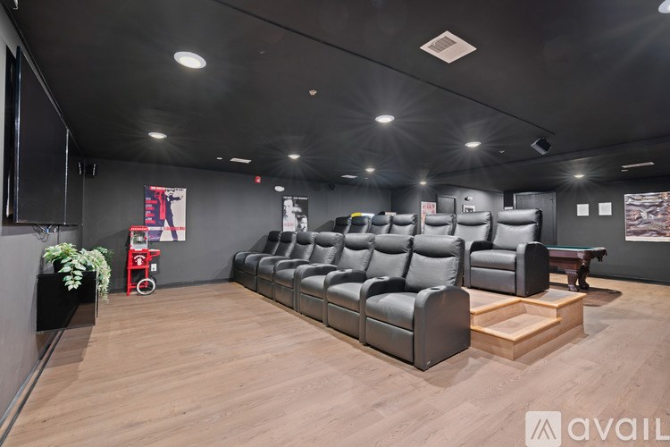 A modern home theater with a row of black leather seats and a wooden floor.