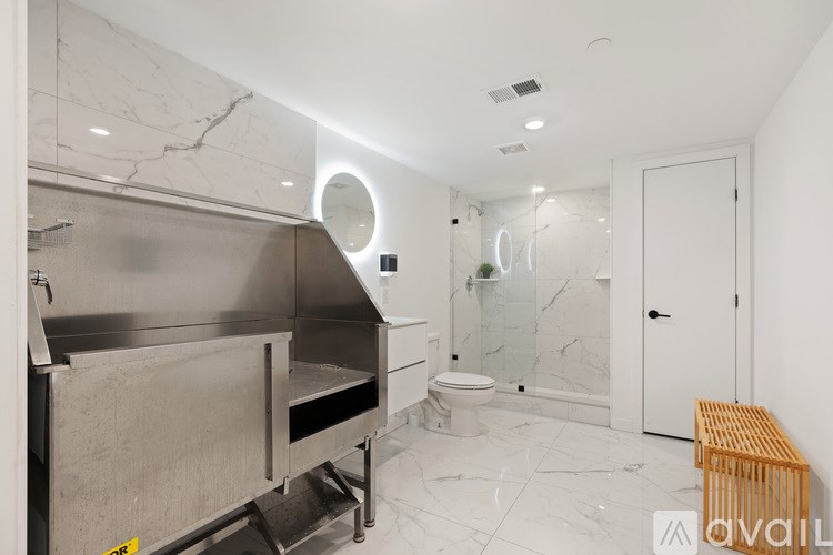 A bathroom with marble floors and walls, a toilet, a sink, and a wooden bench.